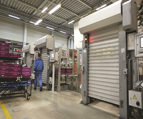 An installed metallic rolling door beside a production workstation.